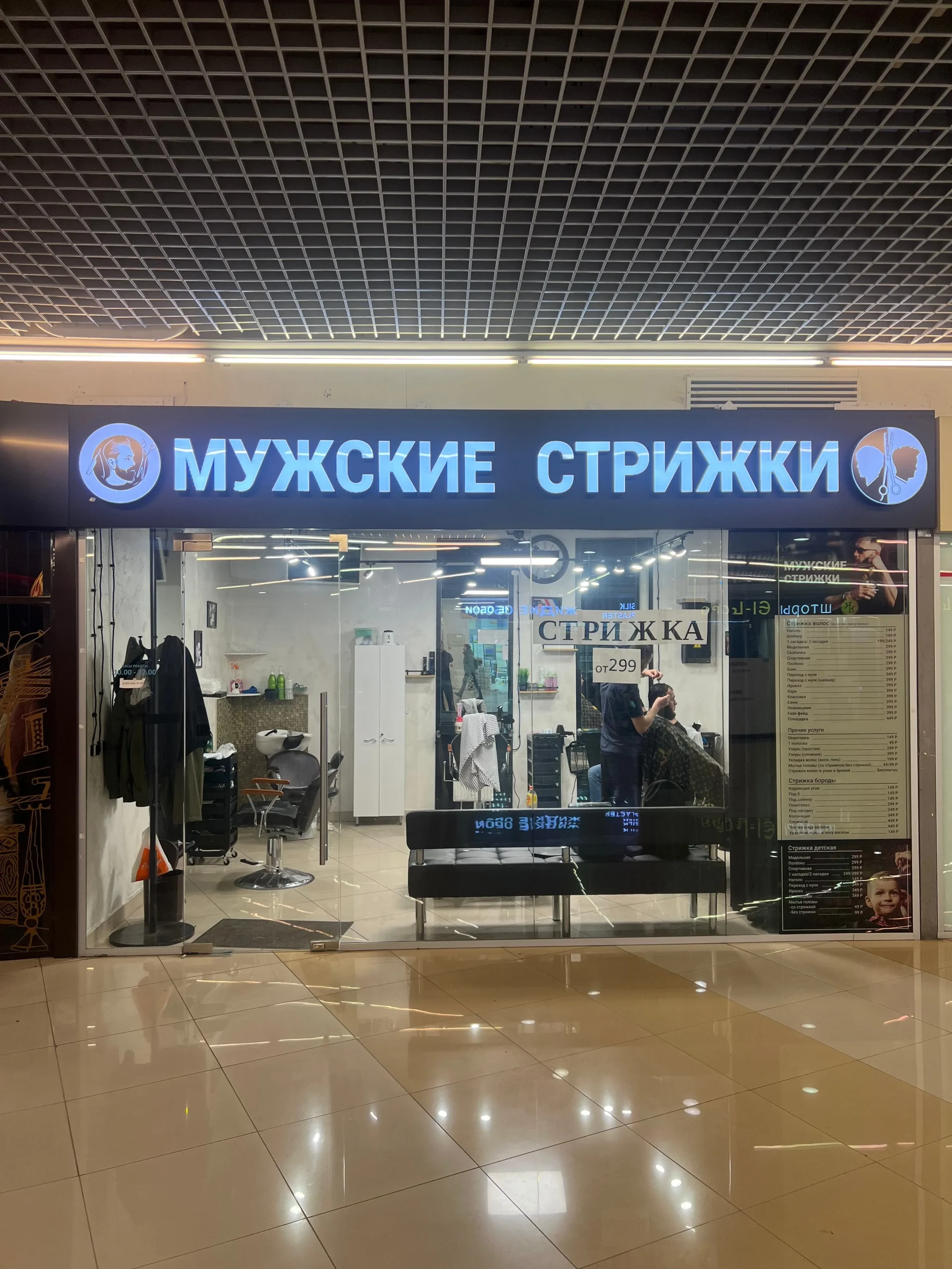 Интерьер современной парикмахерской для мужчин с мастером, выполняющим точную стрижку машинкой и ножницами