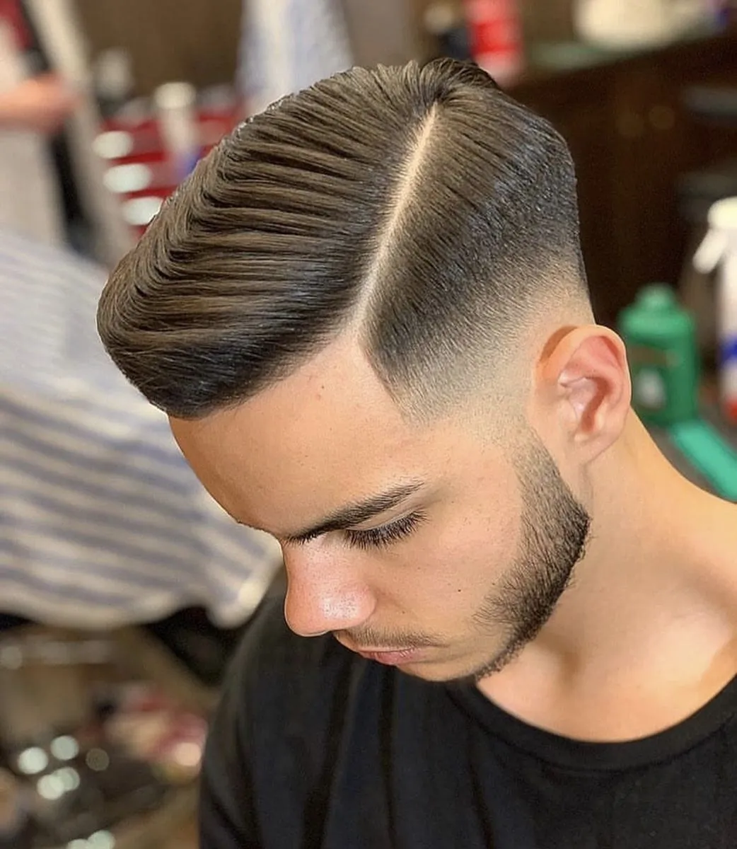 Профессиональный парикмахер мужской выполняет стрижку и оформление бороды клиенту в современном барбершопе