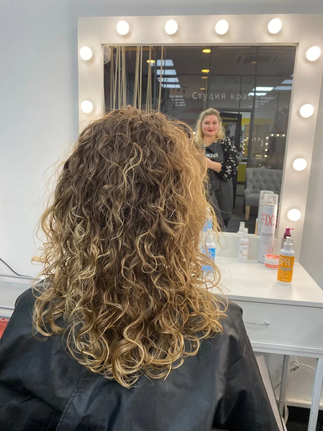 Процесс выполнения японской завивки волос в салоне: мастер наносит специальный состав на пряди